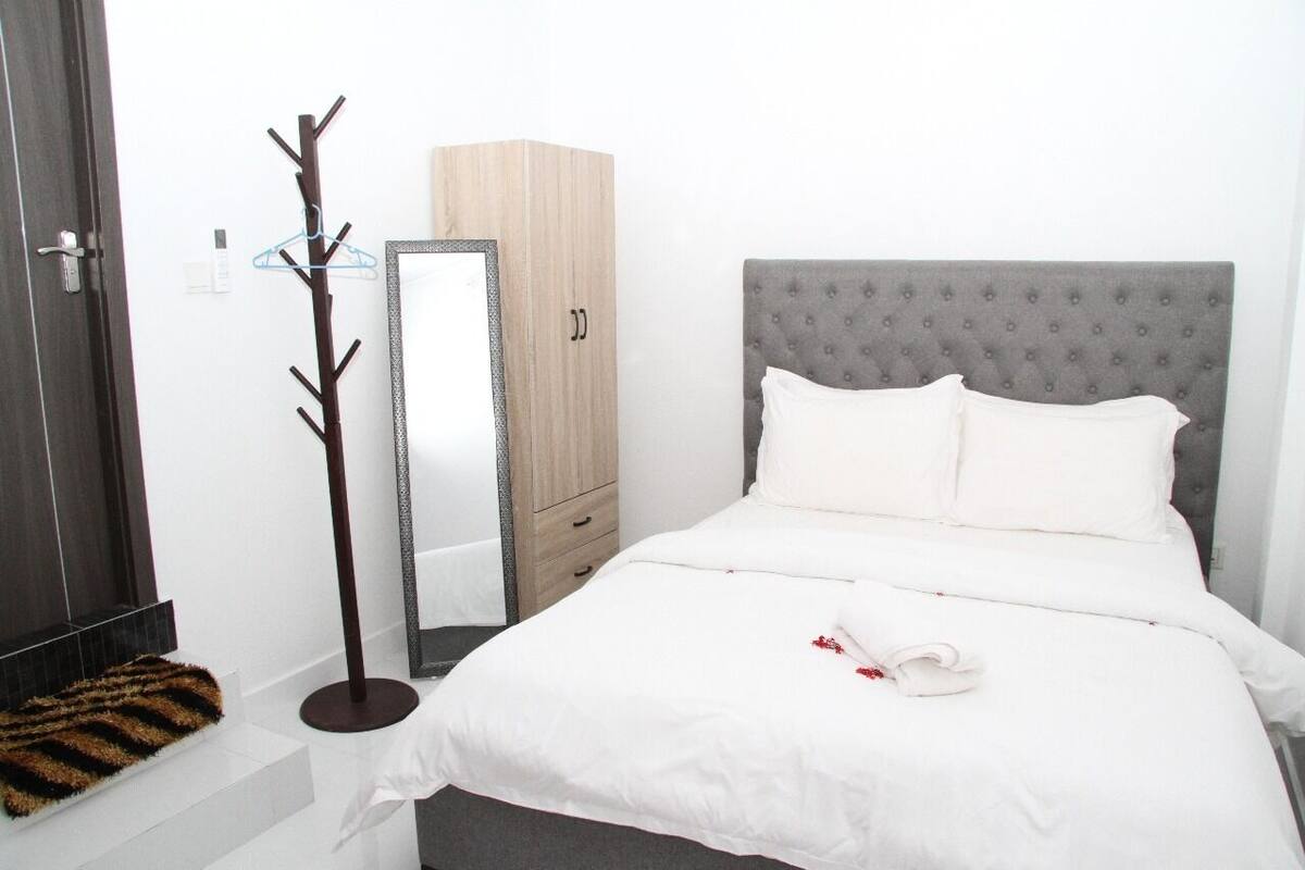 Habitación de hotel ordenada con cama, armario, perchero y espejo.