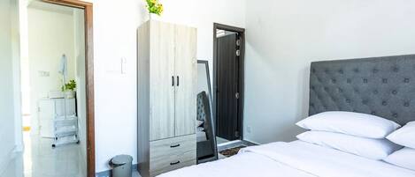 A modern bedroom with a large bed, a grey tufted headboard, a wooden wardrobe, and a mirror.