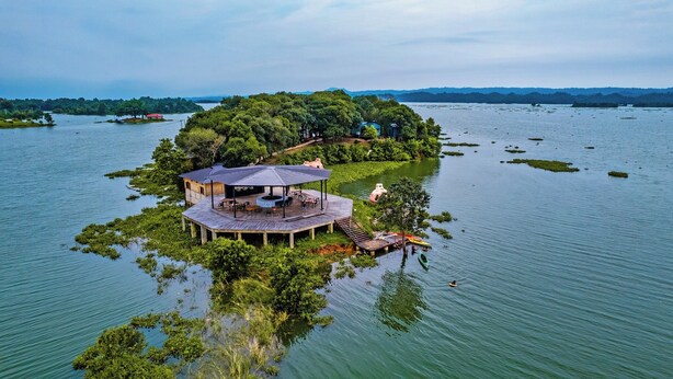 Una isla apartada con una estructura de madera que incluye una terraza abierta y una zona de estar, rodeada de agua y vegetación.