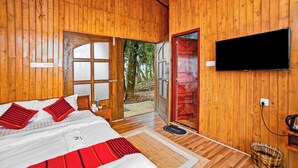 Una habitación de madera con una cama, un televisor y una puerta que da al exterior.