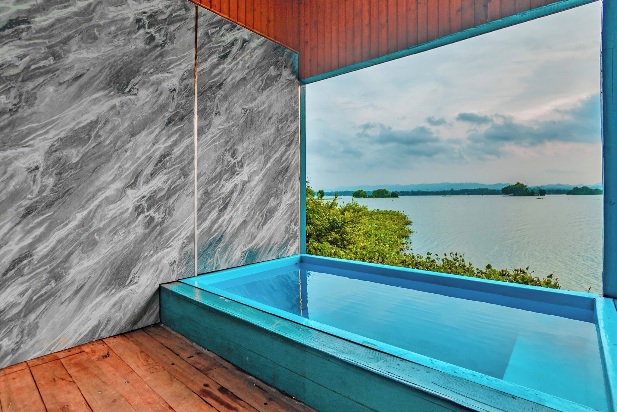 A modern room with a large window overlooking a lake, a wooden floor, and a marble wall.