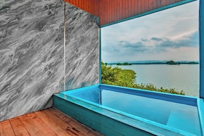 A modern room with a large window overlooking a lake, a wooden floor, and a marble wall.