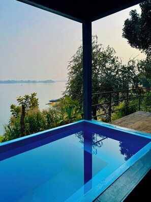 Vista despejada de una piscina con fondo de vidrio, rodeada de abundante vegetación y con vista a una masa de agua tranquila.