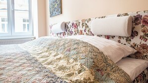 Un letto con testiera floreale, una coperta e una finestra vista edifici.