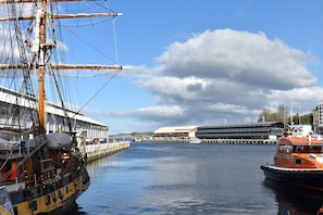 Un port où est amarré un grand voilier, un bâtiment moderne et un petit bateau orange.