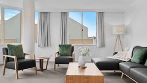 Una habitación de hotel moderna con sofá, dos sillones, una mesita de centro y una lámpara de pie.
