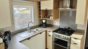 A compact kitchen with a sink, stove, and oven, a coffee maker, and a window with a view of the outside. - Mobile home "Möwe am Geiseltalsee (Mücheln (Geiseltal))