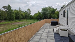A covered outdoor area with a wooden fence, stone flooring, and planters. - Mobile home "Möwe am Geiseltalsee (Mücheln (Geiseltal))