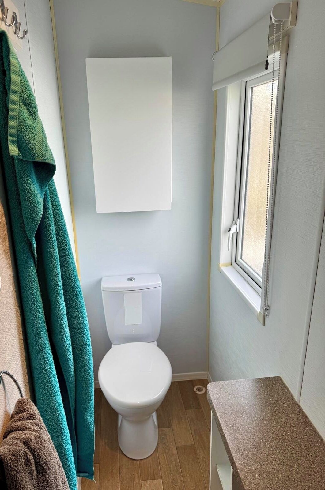 Un baño pequeño con inodoro, toallero con toallas, ventana y una pizarra en la pared.