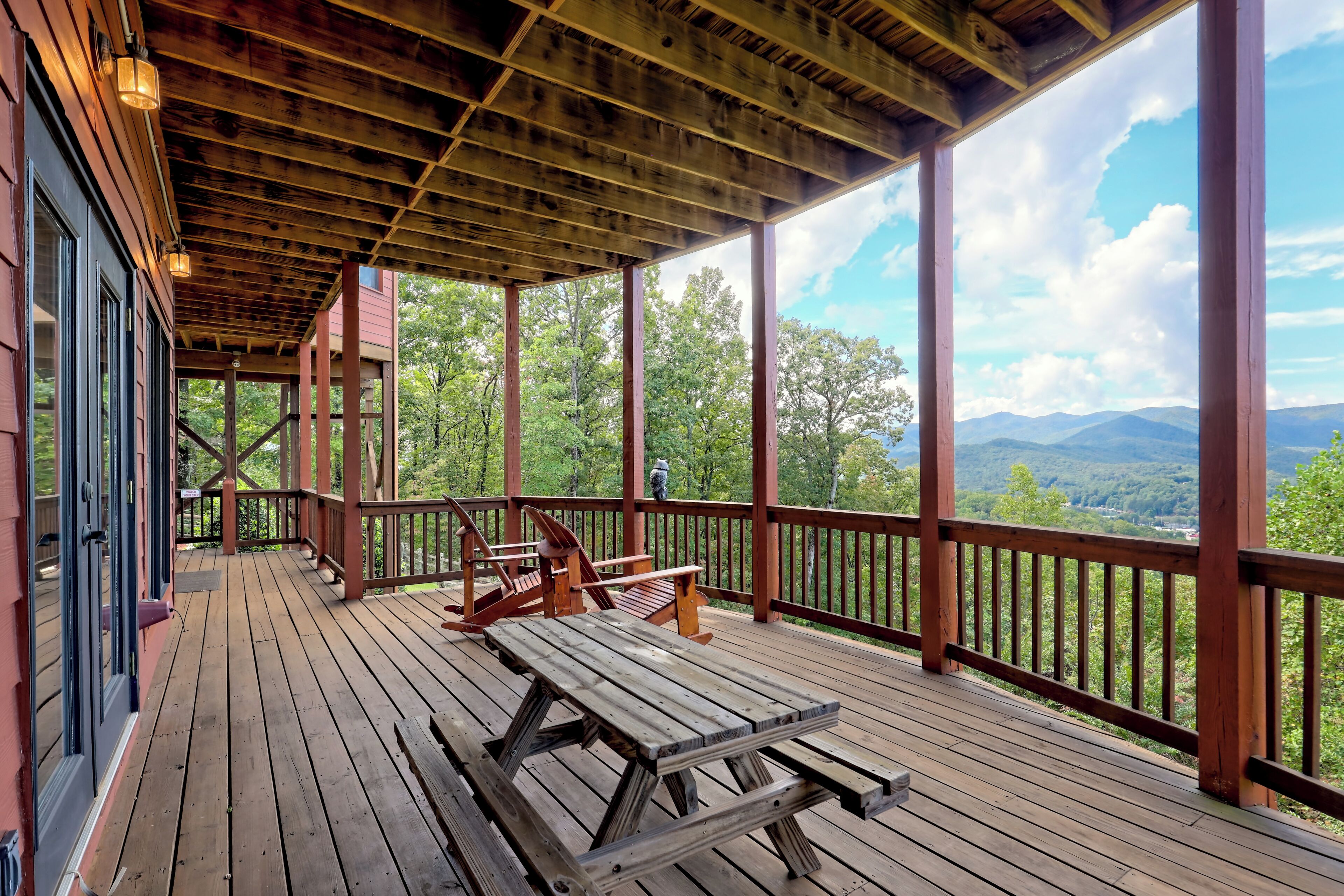 A wooden deck with a picnic table and chairs, overlooking a forested landscape.