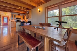 Una mesa de comedor de madera con bancos, un telescopio y una cocina al fondo.