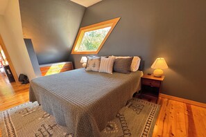 Un dormitorio con una cama grande, un tragaluz, una mesita de noche con lámpara y suelo de madera.
