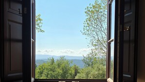 Puerta abierta que da a un balcón con vistas a zonas verdes y montañas a lo lejos.