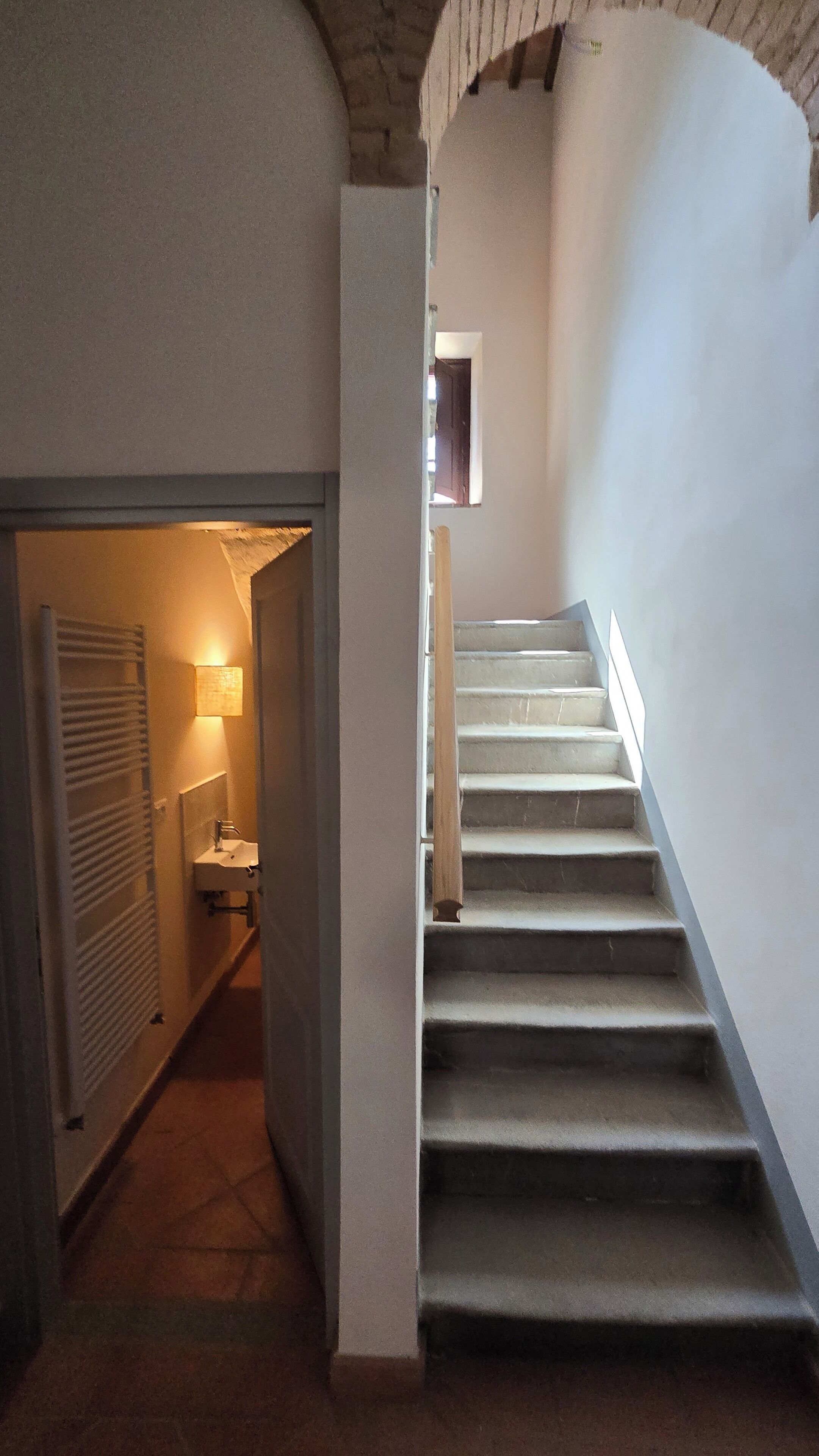 A staircase with a handrail, a small window at the top, and a door leading to a bathroom with a towel rack.