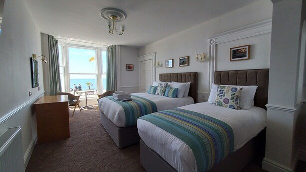 A hotel room with two beds, a small desk, and a view of the sea. - Richmond Hotel (Aberystwyth)