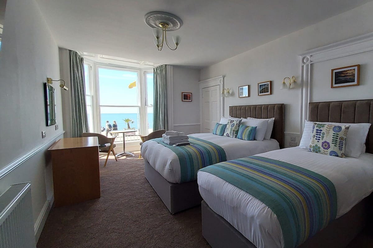 A hotel room with two beds, a small desk, and a view of the sea.