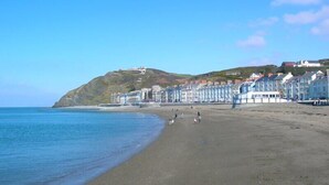 A coastal beach with a row of colorful houses and a hill with a building on top. - Richmond Hotel (Aberystwyth)