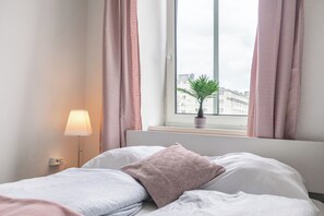 Una camera d'albergo con un letto, una lampada da comodino, una finestra con tende e vista sugli edifici.