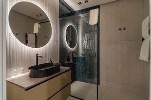 Un baño moderno con un espejo redondo, un lavabo y una cabina de ducha de vidrio.