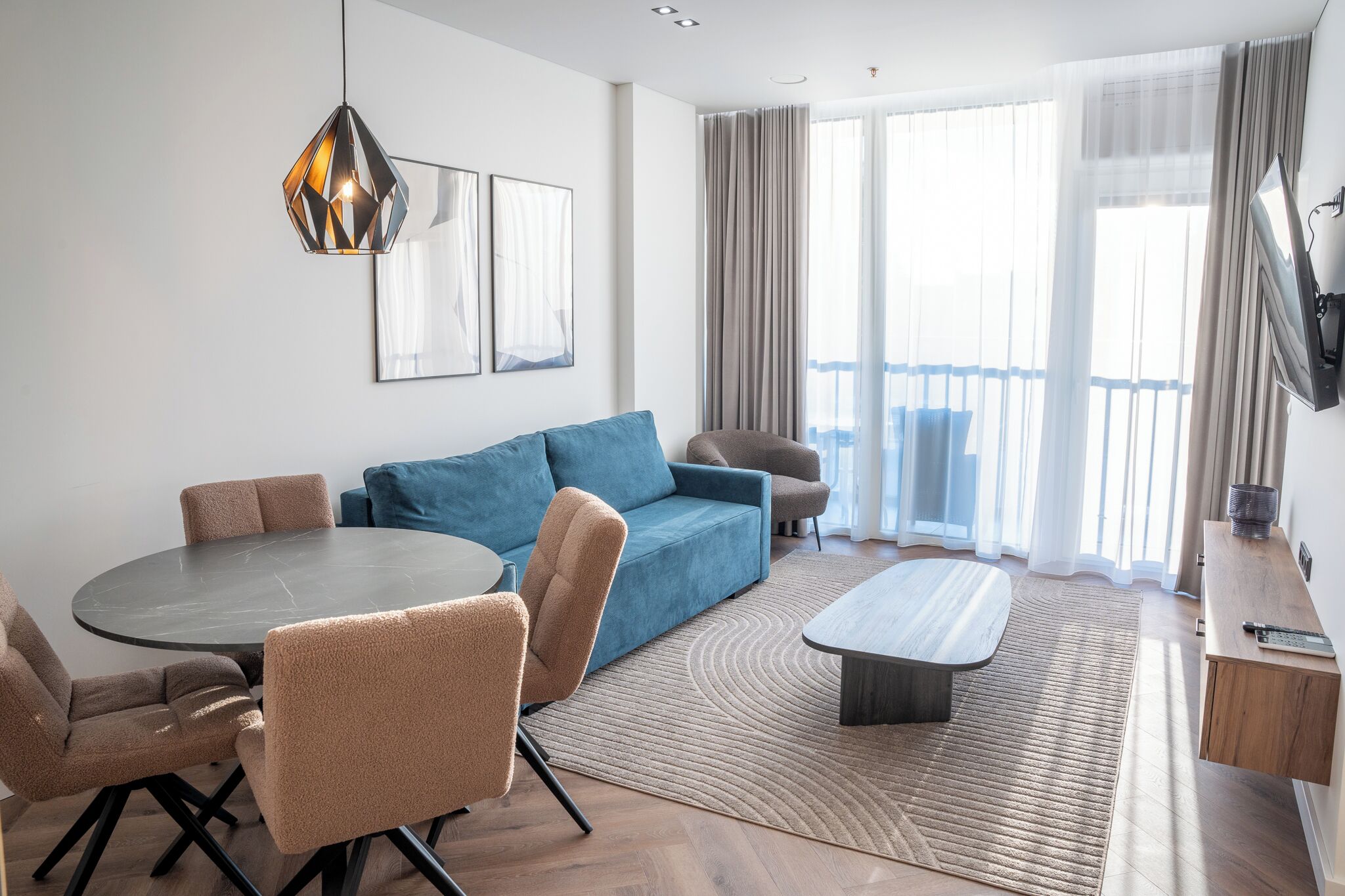 A modern living room with a round dining table, sofas, and a flat-screen TV.