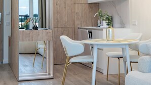 A modern kitchen with a white countertop, a dining area with white chairs, and a large mirror reflecting the room. - Nemunas Aparthotel (Druskininkai)