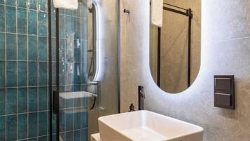 Un baño moderno con ducha de vidrio, un espejo grande y un tocador de madera con lavabo.
