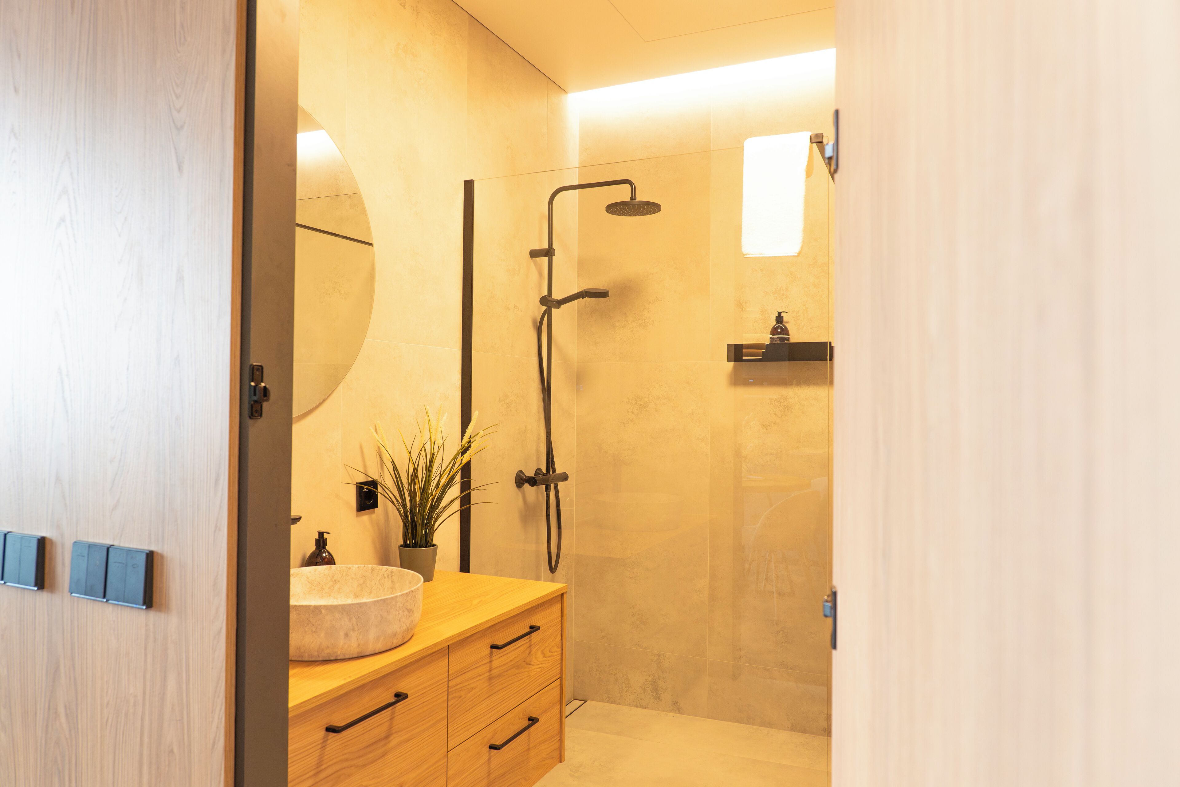 A modern bathroom with a wooden vanity, a round sink, a mirror, and a shower area.