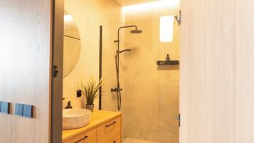A modern bathroom with a wooden vanity, a round sink, a mirror, and a shower area.
