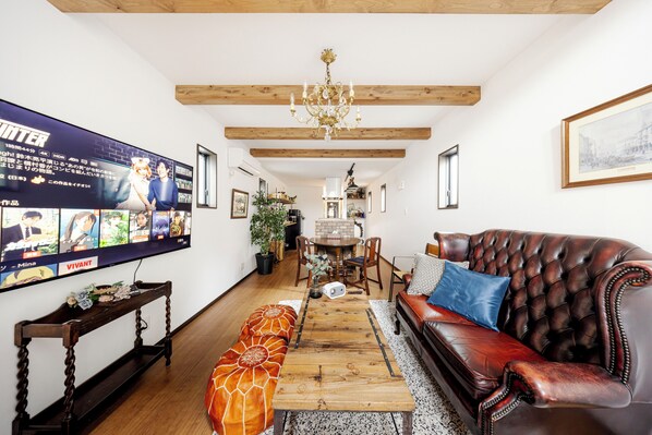 A living room with a wooden coffee table, a leather sofa, a TV mounted on the wall, and a chandelier.