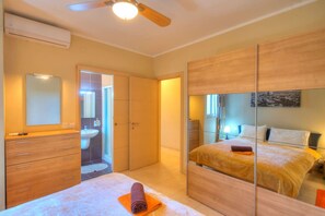 Een moderne slaapkamer met een bed, nachtkastje, spiegel, kledingkast en een badkamer met wastafel en douche.
