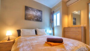 A hotel room with a bed, a nightstand, a dresser, a mirror, and a painting on the wall. - Spacious Apartment with Pool in Misrah Simar, Qala (Qala)