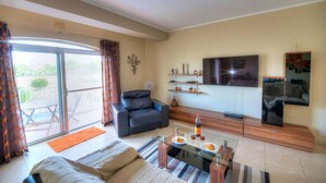 A living room with a sofa, a coffee table with plates, a TV, and a ceiling fan. - Spacious Apartment with Pool in Misrah Simar, Qala (Qala)
