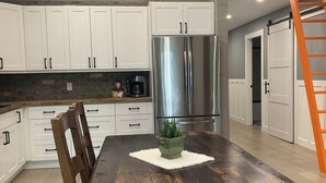 A spacious kitchen with white cabinets, a stainless steel refrigerator, and a wooden dining table. - Oceanfront Views, Full Kitchen,  Wi-Fi ~ Where the Forest Meets the Ocean (Galiano Island)