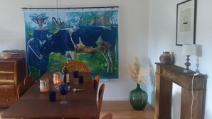 A dining area with a wooden table, chairs, a vase with flowers, a candle, and a painting of a cow and deer on the wall.