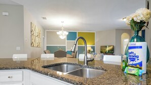A modern kitchen with granite countertops, a stainless steel sink, and white cabinetry. There is a vase with flowers on the counter and a package of paper towels. - 20 min to Disney , Epic , Star Wars , Gameroom ,Pool Luxe dw7 (Davenport)