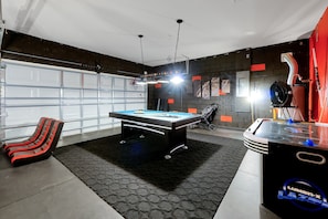 A pool table in a room with a garage door, a red and black lounge chair, and a table tennis table. - 20 min to Disney , Epic , Star Wars , Gameroom ,Pool Luxe dw7 (Davenport)