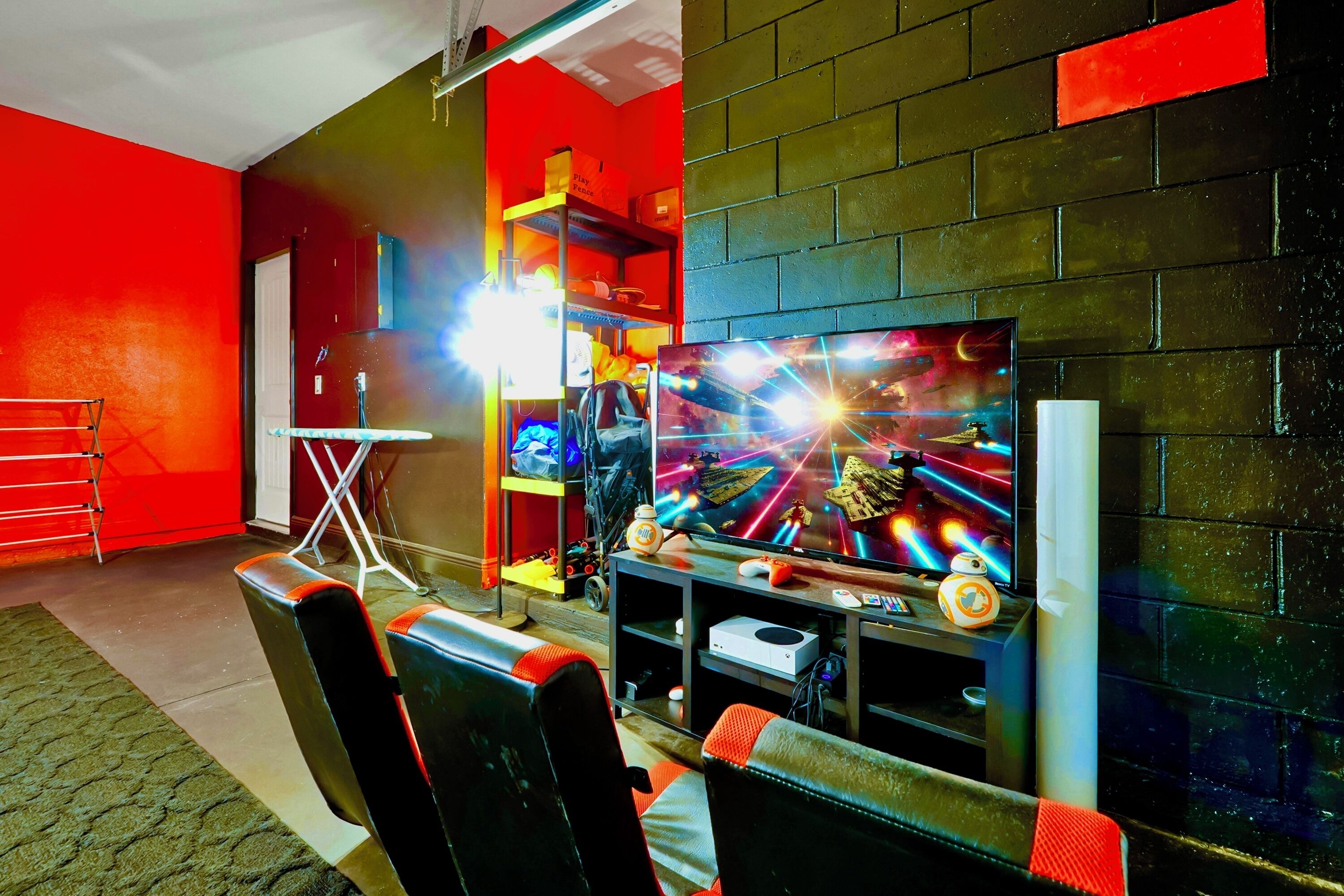 A gaming room with a large TV, gaming chairs, and shelves with gaming equipment.