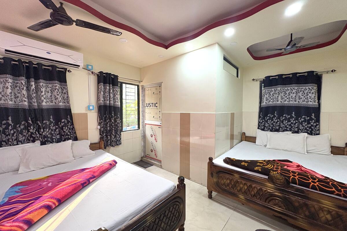 A hotel room with two beds, a ceiling fan, an air conditioning unit, and a window with curtains.