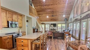 A spacious kitchen with wooden cabinets, a large island, and a dining area with wooden furniture. - Private Beaver Lake front Escape | 50 Acres (Rogers)