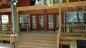 A wooden cabin with a porch, red doors, and a staircase leading to the entrance. - Private Beaver Lake front Escape | 50 Acres (Rogers)