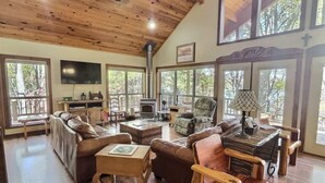 A spacious living room with a wooden ceiling, large windows, a fireplace, and leather furniture. - Private Beaver Lake front Escape | 50 Acres (Rogers)