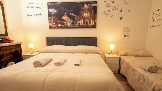 Ein Hotelzimmer mit einem großen Bett, zwei Nachttischen mit Lampen, einem Beistelltisch, einer Kommode und einer Wand mit inspirierenden Zitaten und einem Stadtbild.