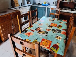 Una cucina con mobili in legno, una lavatrice e un tavolo ricoperto da una tovaglia con immagini di cibo e bevande.