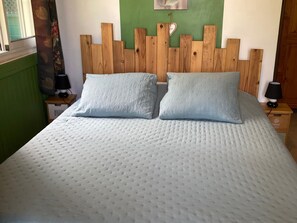 A bed with a quilted white cover, two pillows, a wooden headboard with a heart-shaped decoration, and a nightstand with a lamp. - Authentic Creole Room in Les Avirons (Les Avirons)