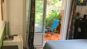 A bedroom with a bed, a desk with a computer, and a chair. There is a window with curtains, and a chair outside the window. - Authentic Creole Room in Les Avirons (Les Avirons)