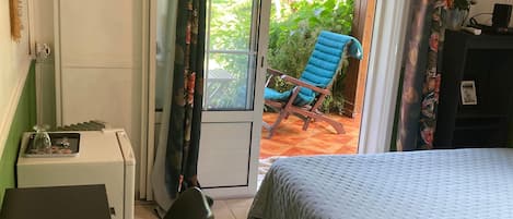 Un dormitorio con una cama, un escritorio, una silla y vistas al exterior a través de una puerta.