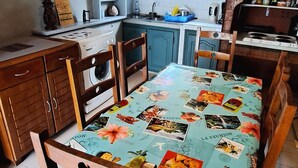 A kitchen with wooden cabinets, a washing machine, and a table covered with a tablecloth featuring food and drink images. - Authentic Creole Room in Les Avirons (Les Avirons)