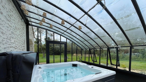 Ein Whirlpool in einem Gewächshaus mit Glasdach, umgeben von einem Garten.