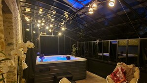 Ein Whirlpool in einem überdachten Außenbereich mit Lichterketten, einem Stuhl und einer Decke.