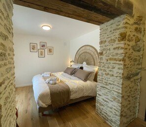 Un dormitorio con pared de piedra, vigas de madera, cama con almohadas y una colcha, y cuadros enmarcados en la pared.